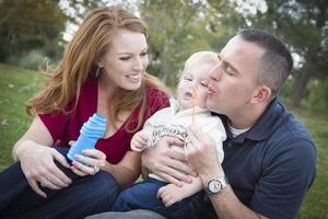 Young Parents Blowing Bubbles with their Child Boy in Park photo