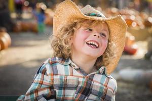 niño pequeño con sombrero de vaquero en el huerto de calabazas foto