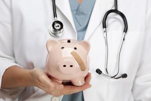 Doctor Holding Piggy Bank with Bandage on Face photo