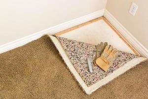 Gloves and Utility Knife On Pulled Back Carpet and Pad In Room. photo