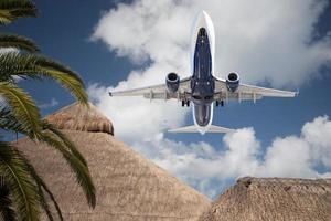Bottom View of Passenger Airplane Flying Over Tropical Palm Trees and Huts photo