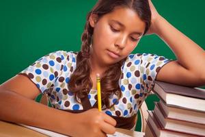 estudiante hispana con lápiz y libros estudiando con pizarra detrás foto