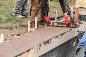 Construction Workers Pouring And Leveling Wet Cement Into Wood Framing photo