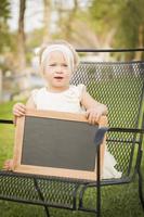 linda niña en una silla sosteniendo una pizarra en blanco foto