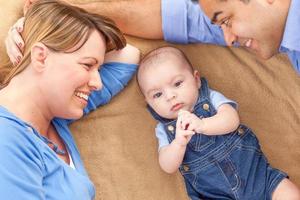 Young Mixed Race Couple Laying With Their Infant On A Blanket photo