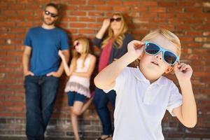 Cute Young Caucasian Boy Wearing Sunglasses with Family Behind photo