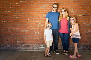 Young Caucasian Family Wearing Sunglasses Against Brick Wall photo