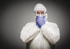 Man Covering Mouth With Hands Wearing HAZMAT Protective Clothing Against A Gray Background. photo