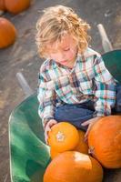 Little Boy Sitting in a Wheelbarrow Next to His Pumpkins in a Rustic Ranch Setting at the Pumpkin Patch. photo