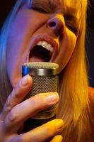 Female vocalist under gelled lighting sings with passion into condenser microphone. photo