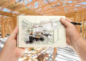Male Hands Holding Pen and Pad of Paper with Custom Kitchen Illustration Inside Construction Framing. photo