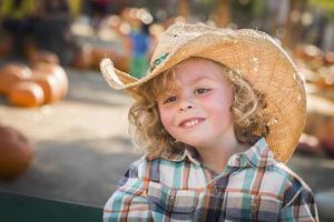 niño pequeño con sombrero de vaquero en el huerto de calabazas foto