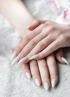 manos de una mujer joven con manicura blanca en las uñas foto