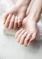 manos de una mujer joven con manicura blanca en las uñas foto