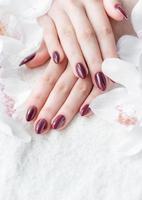 manos de una mujer joven con manicura roja oscura en las uñas foto