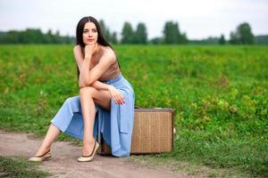 Beautiful young lady with suitcase on countryside road photo