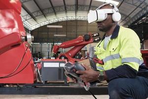 An African American engineer with VR glasses controls robotic arm, virtual simulator software in mechanical manufacturing factory, and intelligent automatic machines technology in industry innovation. photo
