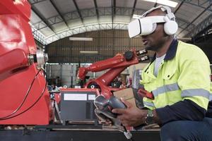 An African American engineer with VR glasses controls robotic arm, virtual simulator software in mechanical manufacturing factory, and intelligent automatic machines technology in industry innovation. photo