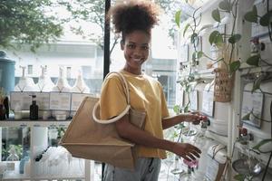 A Black female customer fills liquid soap into recycling jar from reusable containers in a zero-waste and refill store, smiles, and looks at camera, happy shopping in an environment-friendly shop. photo