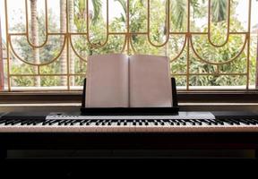 Electric piano with empty sheet music near the big window overlooking green garden, front view photo