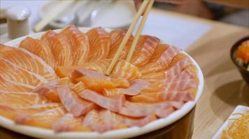 4k video van gebruik makend van eetstokje plukken slamon omhoog van bord vol van Zalm sashimi