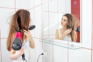 young charming girl stands in front of the mirror room a bit dark entrance and dries hair photo