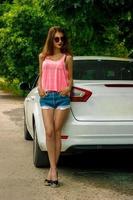 hermosa dama en pantalones cortos y una camiseta rosa parada cerca del auto foto