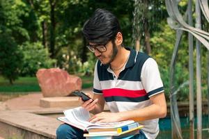 Young brunette student boy with books in hands using a mobile phone photo