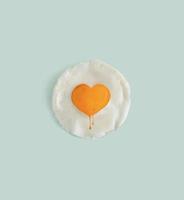 Creative flat lay concept of a poached egg with a yolk in a heart shape. Popular design approach against light pastel mint green color. Valentine's day, love and food theme idea. photo