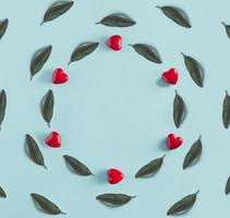 Creative circle arrangemen with red hearts and  green leaves on a blue background. Valentines day and spring concept with copy space. Flat lay. Minimal nature. photo