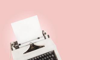 Typewriter with blank paper as a copy space. Retro concept against pink background. Vintage flair stylized composition. photo