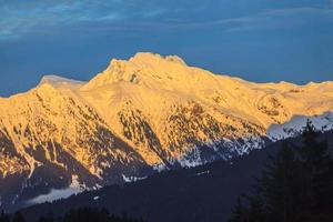 Snow covered mountain top is illuminated by unending sun photo