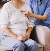 Homecare nursing service and elderly people cardiology healthcare. Close up of young hispanic female doctor nurse check mature caucasian man patient heartbeat using stethoscope during visit photo