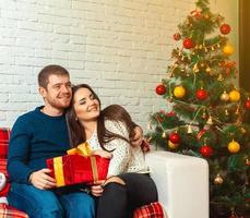 Ceerful couple with christmas gifts sits on couch photo