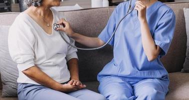 Homecare nursing service and elderly people cardiology healthcare. Close up of young hispanic female doctor nurse check mature caucasian man patient heartbeat using stethoscope during visit photo