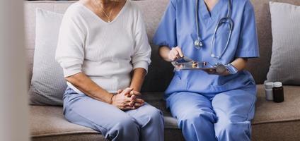 Homecare nursing service and elderly people cardiology healthcare. Close up of young hispanic female doctor nurse check mature caucasian man patient heartbeat using stethoscope during visit photo