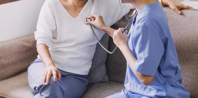 Homecare nursing service and elderly people cardiology healthcare. Close up of young hispanic female doctor nurse check mature caucasian man patient heartbeat using stethoscope during visit photo