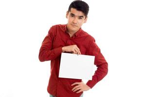 un joven apuesto con camisa roja y una pancarta vacía en las manos posando aislado de fondo blanco foto