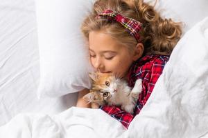 una linda niña duerme dulcemente en casa en un conejo con un gatito. ropa de cama de algodón blanco. vacaciones navideñas. niños y mascotas en casa. foto de alta calidad