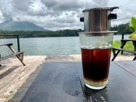 a glass of Vietnamese drip coffee with a lake view in the background photo