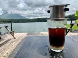 a glass of Vietnamese drip coffee with a lake view in the background photo