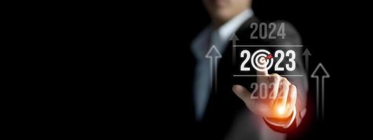 Businessman pointing the concept of the New Year 2023, Business financial and Technology goals and planning for Next Year, Hand pressing increase arrow graph future growth year 2022 to 2023 photo