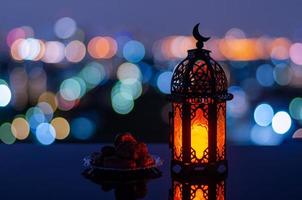 Selective focus of lantern that have moon symbol on top and small plate of dates fruit with city bokeh light background for the Muslim feast of the holy month of Ramadan Kareem. photo