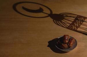 Dates palm fruit put on wooden table with shadow of the lantern that have moon symbol on top for the Muslim feast of the holy month of Ramadan Kareem. photo