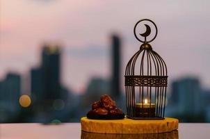 linterna que tiene el símbolo de la luna en la parte superior y dátiles puestos en una bandeja de madera con fondo de ciudad para la fiesta musulmana del mes sagrado de ramadán kareem. foto