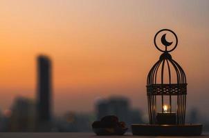 Lantern that have moon symbol on top and small plate of dates fruit with dusk sky and city background for the Muslim feast of the holy month of Ramadan Kareem. photo