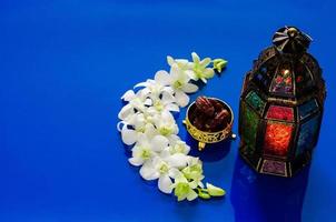 linterna sobre fondo azul con dátiles fruta en flor de orquídea en forma de media luna para la fiesta musulmana del mes sagrado de ramadán kareem. foto