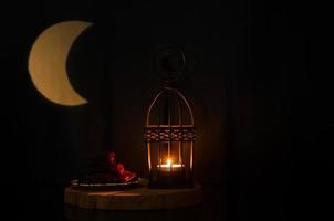 Lantern and small plate of dates fruit on wooden tray with moon shape from light on background for the Muslim feast of the holy month of Ramadan Kareem. photo