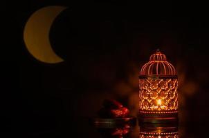 enfoque selectivo de la linterna y un pequeño plato de dátiles con forma de luna de luz en el fondo para la fiesta musulmana del mes sagrado de ramadán kareem. foto