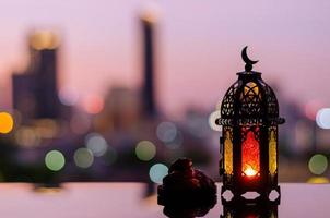 Lantern that have moon symbol on top and small plate of dates fruit with dawn sky and city bokeh light background for the Muslim feast of the holy month of Ramadan Kareem. photo